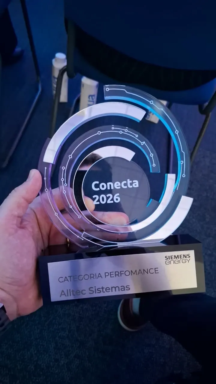 Mão segurando o troféu Conecta 2026, da Siemens Energy: anéis de acrílico com detalhes azuis, base preta e placa da categoria Performance, da Alltec Sistemas