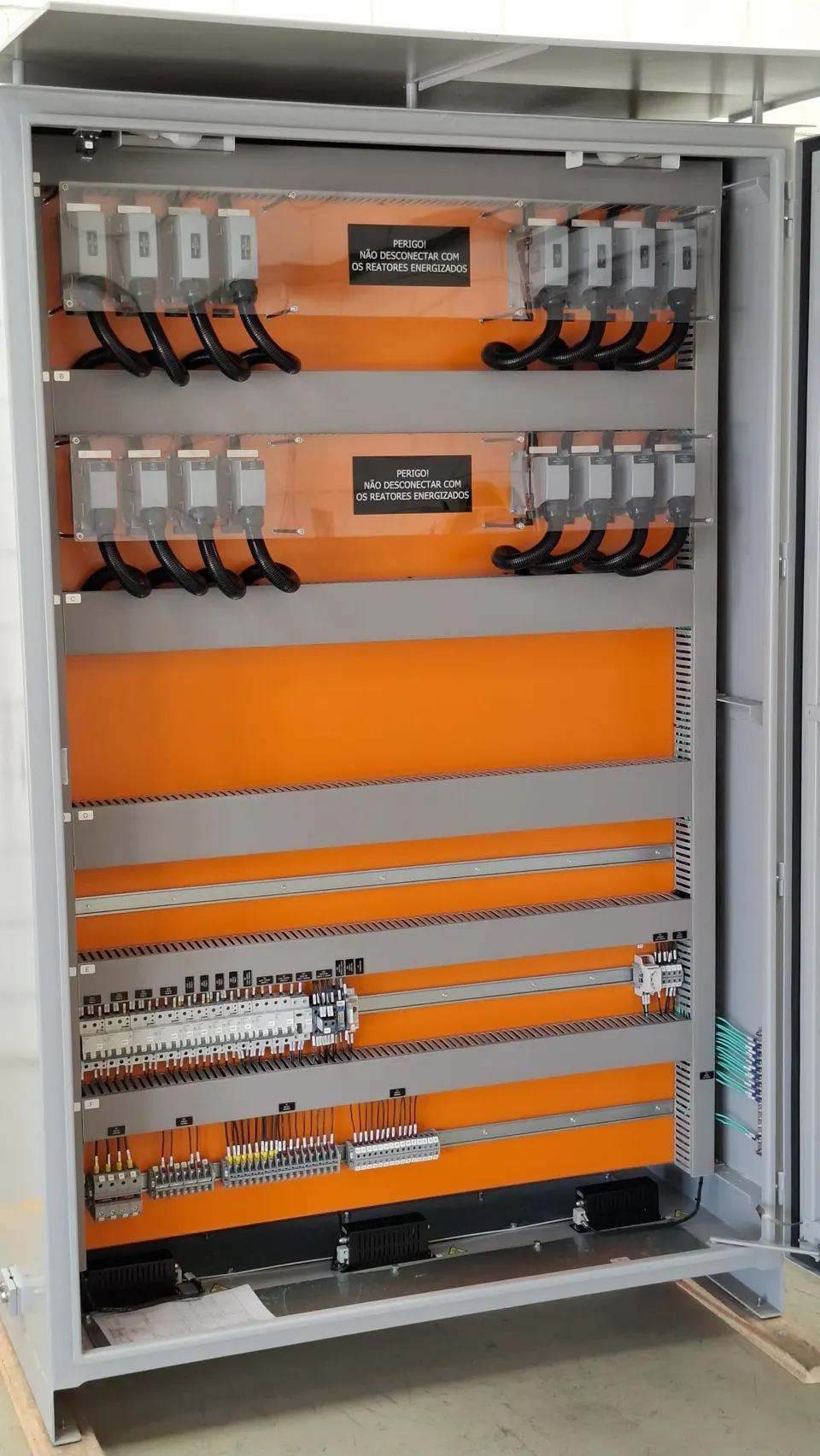 Inside the open cubicle: two rows of multipole connectors behind acrylic, miniature circuit breakers, and terminal strips on an orange mounting plate