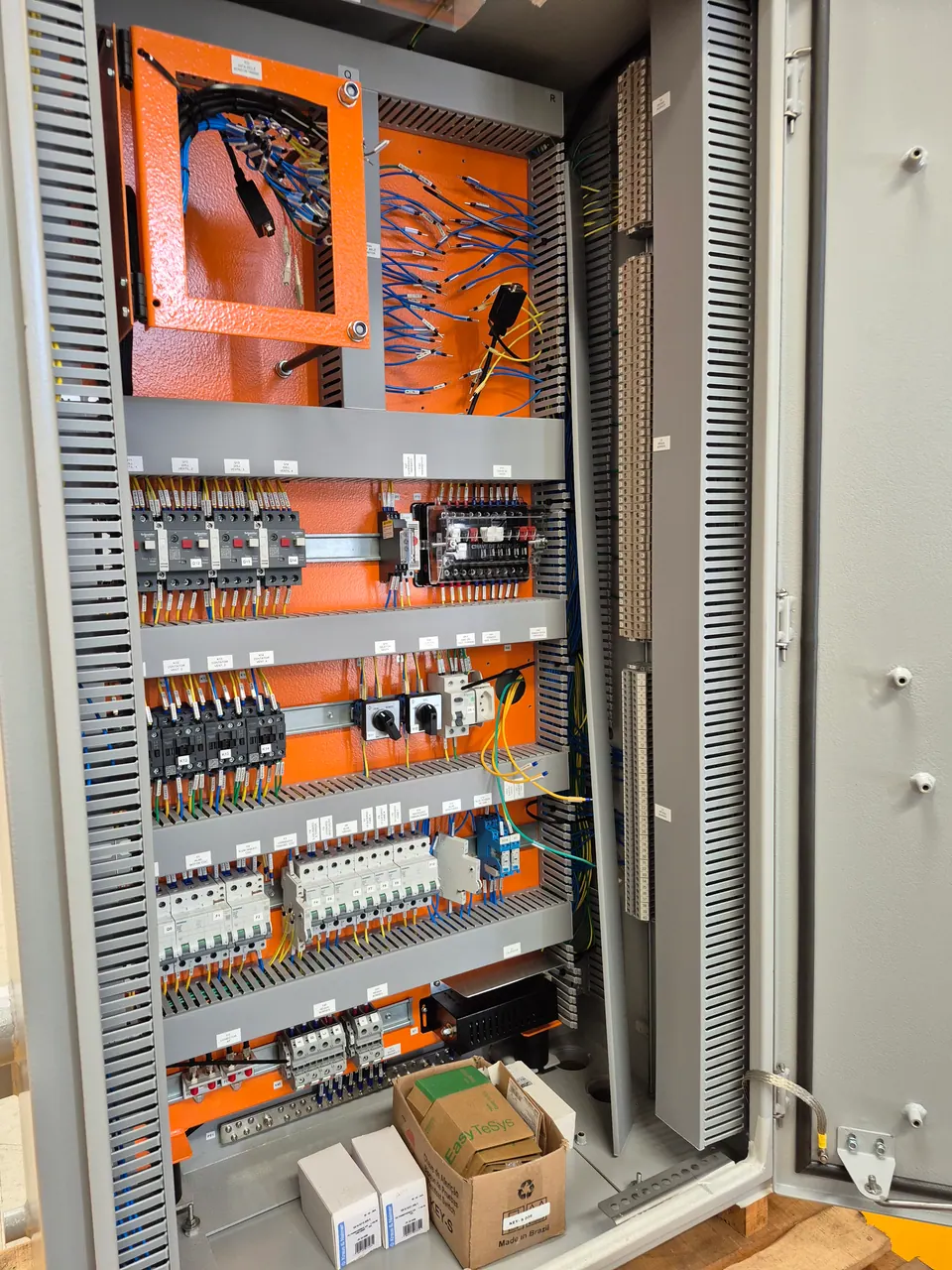 Interior do painel de controle em montagem: moldura articulada para o relé SEL-2414, disjuntores-motor e contatores da ventilação, bornes e canaletas