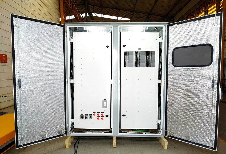 Assembled control cabinet on the factory floor with both outer doors open, lined with foil-faced thermal insulation, and the white inner doors closed and lit from inside