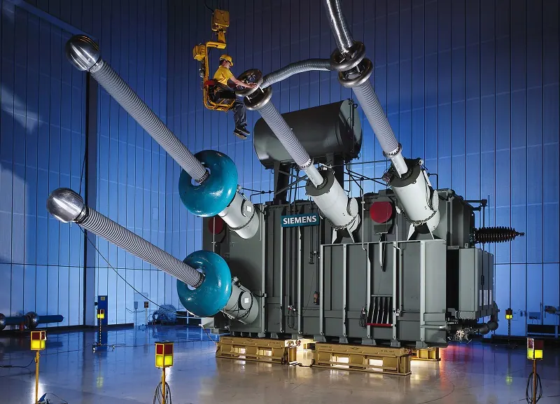 Transformador de potência Siemens com buchas de alta tensão em um laboratório de ensaios, com um técnico em plataforma elevatória junto às buchas